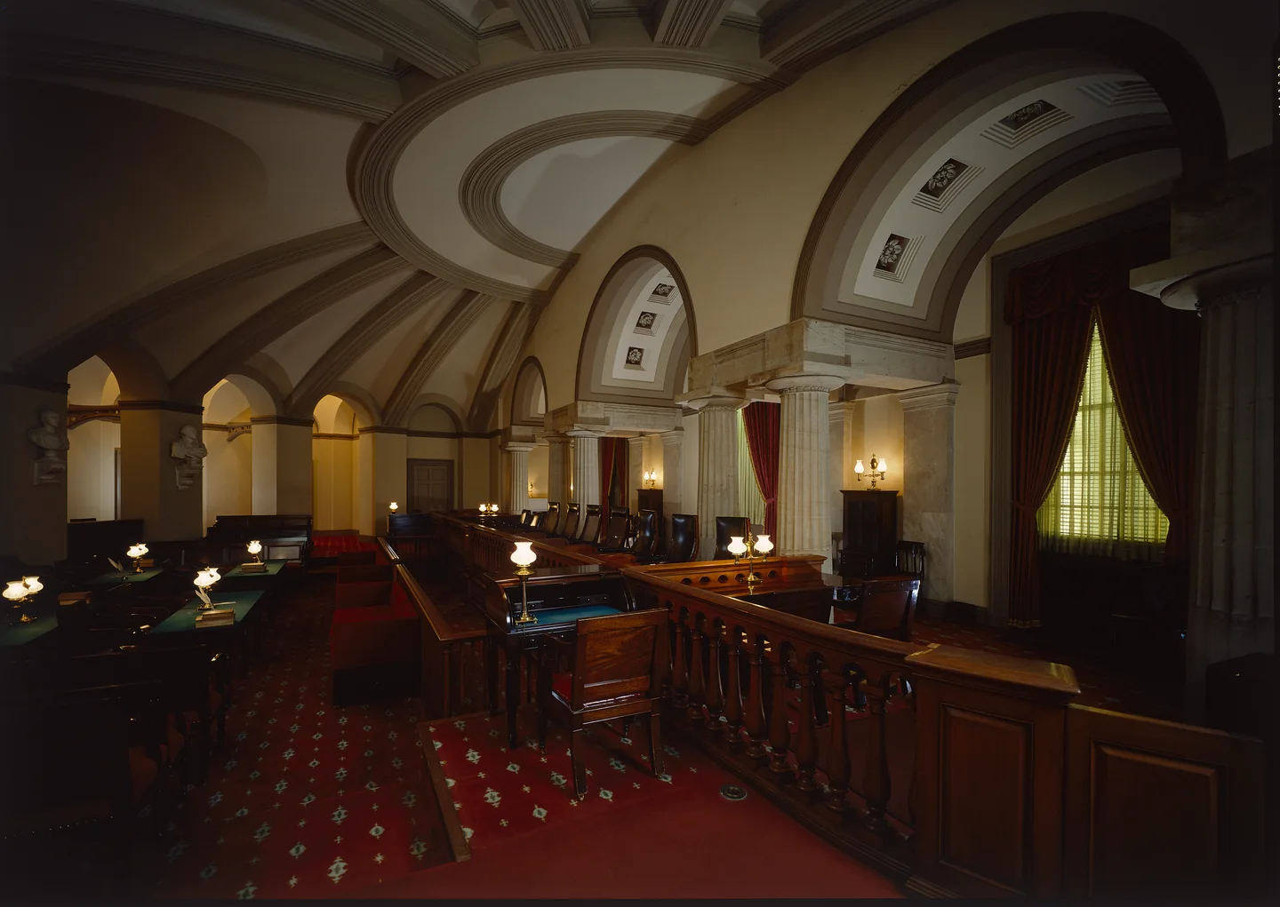 A vaulted courtroom lit by desk lamps, with a carved wooden railing before the bench.
