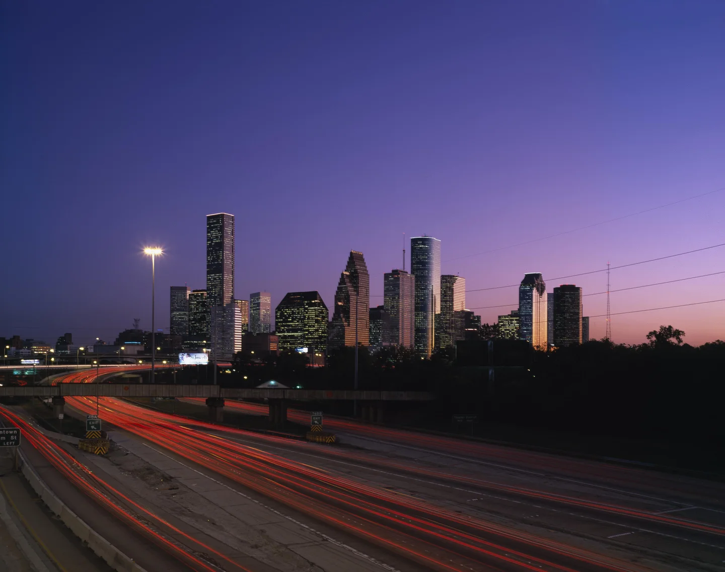 Houston's towers at dusk under a violet sky, traffic streaking in light below.