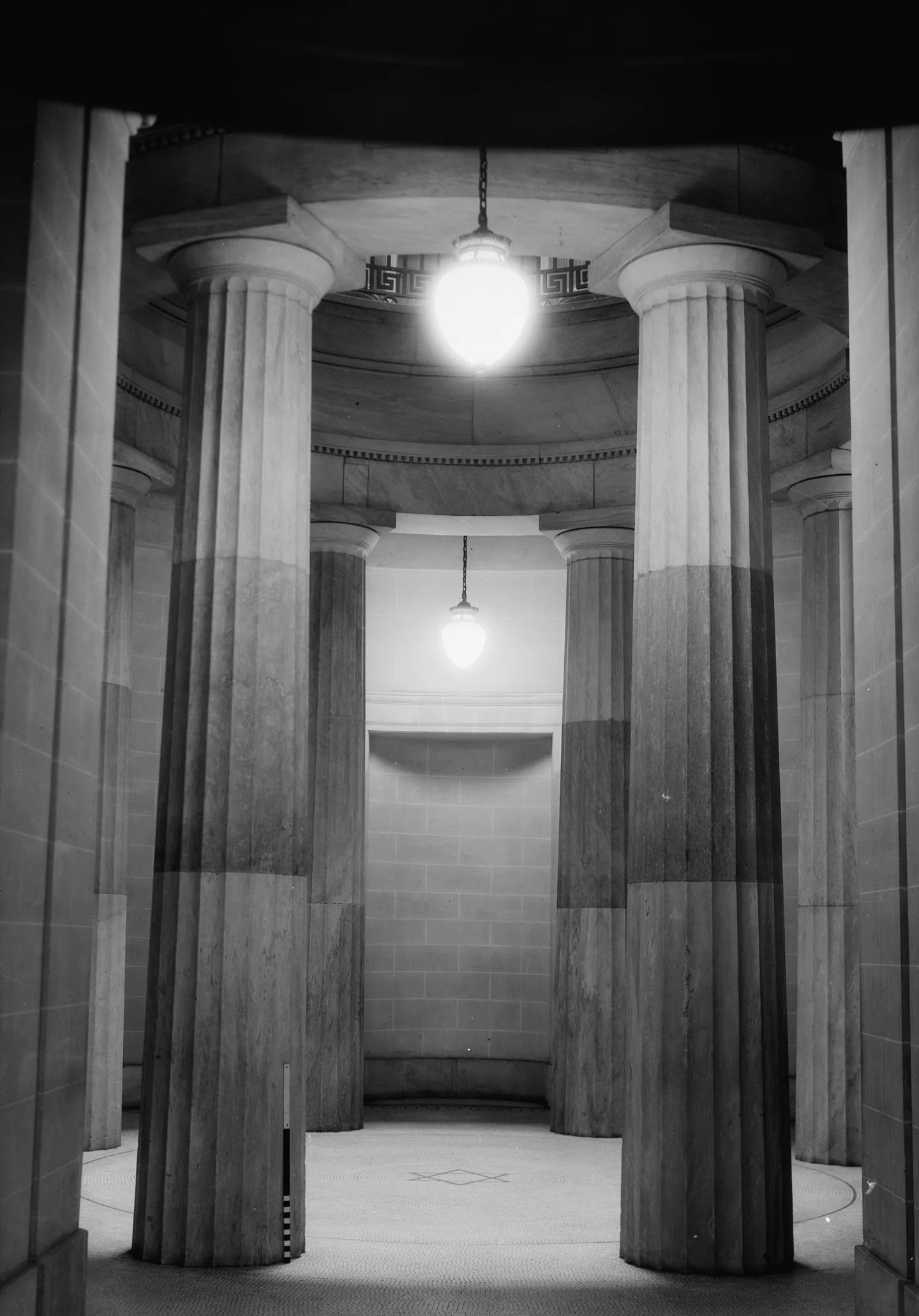 Fluted stone columns in a round hall beneath two hanging lamps.