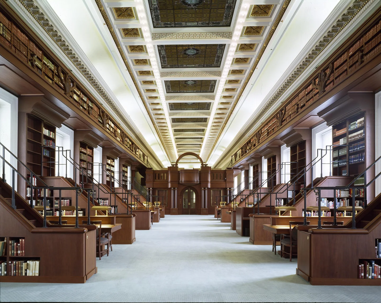 A long reading room of desks and bookcases under a coffered ceiling.