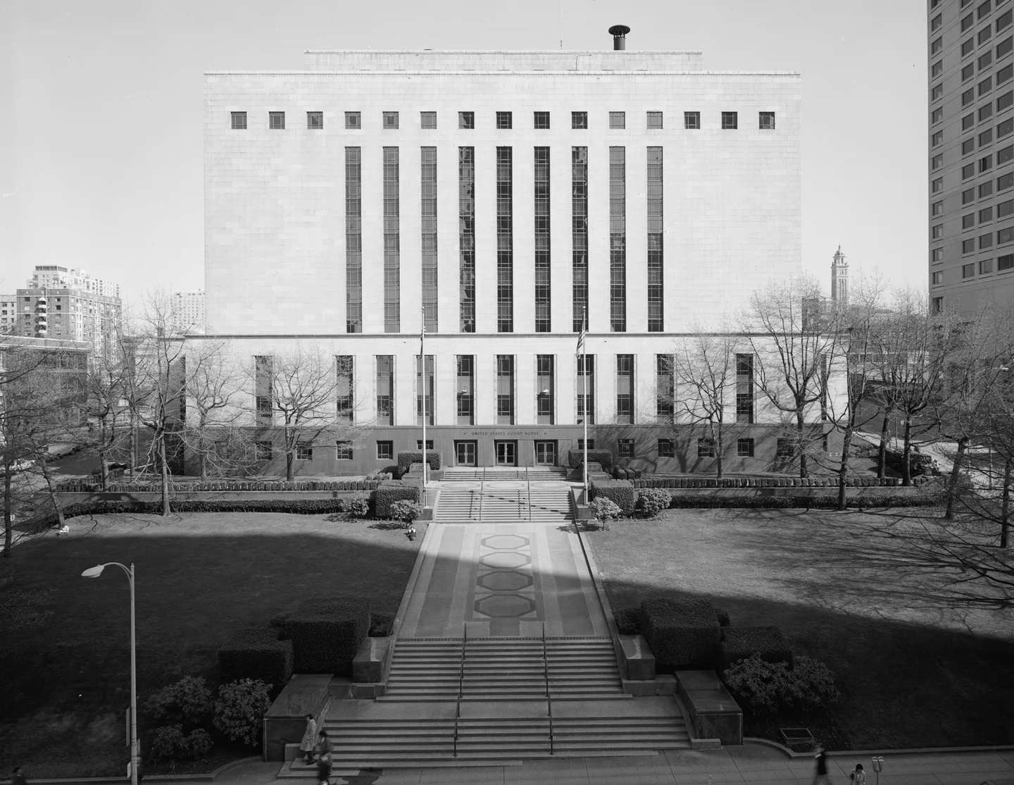 Broad stone steps and a paved walk leading to a tall courthouse with narrow vertical windows.